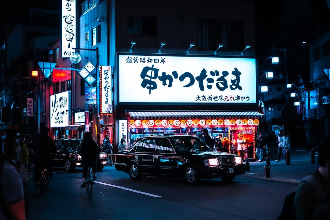 Japanese sedan parked in front of neon lit city street at night